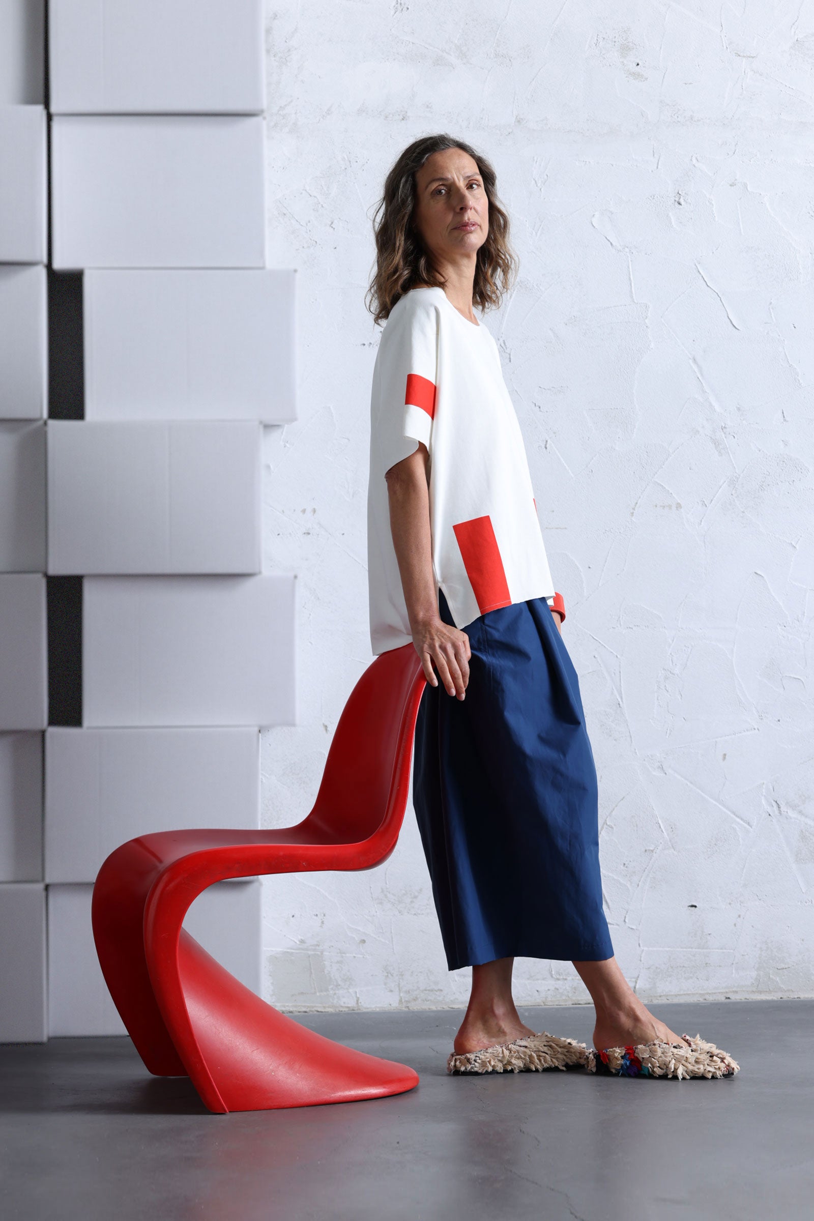 Off-White T-Shirt with red rectangles, model wearing blues pants standing next to a red Panton chair